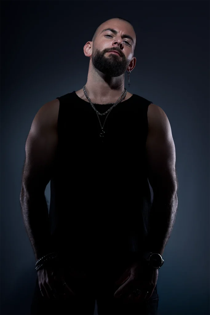 Retrato de DJ Lahox con collares y camiseta negra en estudio fotográfico.