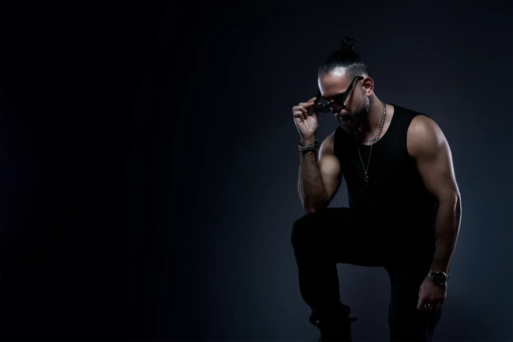 Fotografía de marca personal de DJ Lahox con gafas de sol en estudio. Foto de DJ Lahox en camiseta negra de tirantes sobre fondo rojo con movimiento.